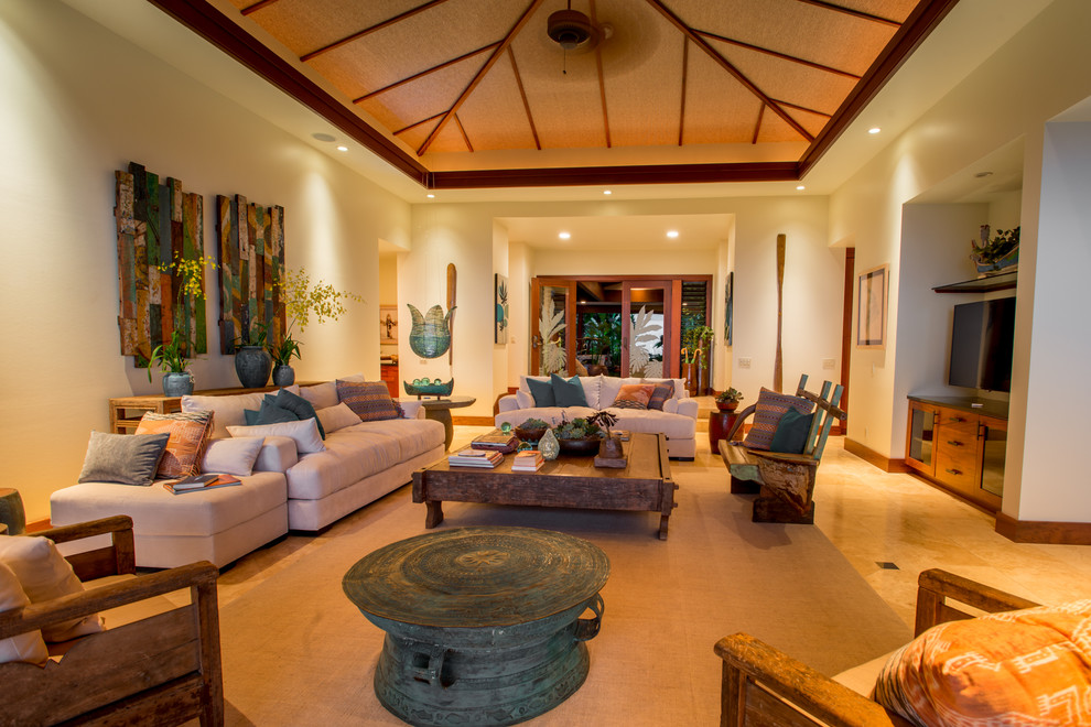 Large tropical open concept living room in Hawaii with white walls, limestone floors and a built-in media wall.