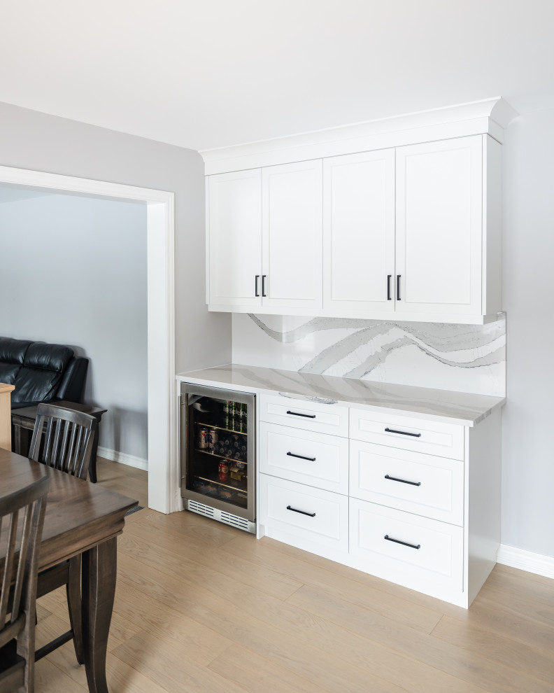 Example of a mid-sized transitional u-shaped light wood floor eat-in kitchen design in Toronto with an undermount sink, shaker cabinets, white cabinets, quartz countertops, white backsplash, quartz backsplash, stainless steel appliances, an island and white countertops