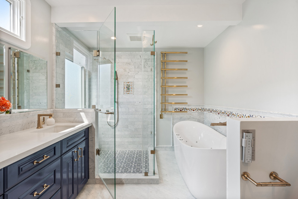 This is an example of a large transitional master bathroom in San Francisco with raised-panel cabinets, blue cabinets, a freestanding tub, a corner shower, a bidet, gray tile, marble, grey walls, marble floors, an undermount sink, engineered quartz benchtops, grey floor, a hinged shower door, white benchtops, a double vanity and a built-in vanity.