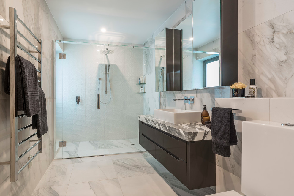 Inspiration for a large contemporary master bathroom in Hamilton with flat-panel cabinets, brown cabinets, a one-piece toilet, porcelain tile, porcelain floors, a vessel sink, marble benchtops, white floor, a hinged shower door, a curbless shower, gray tile and white tile.