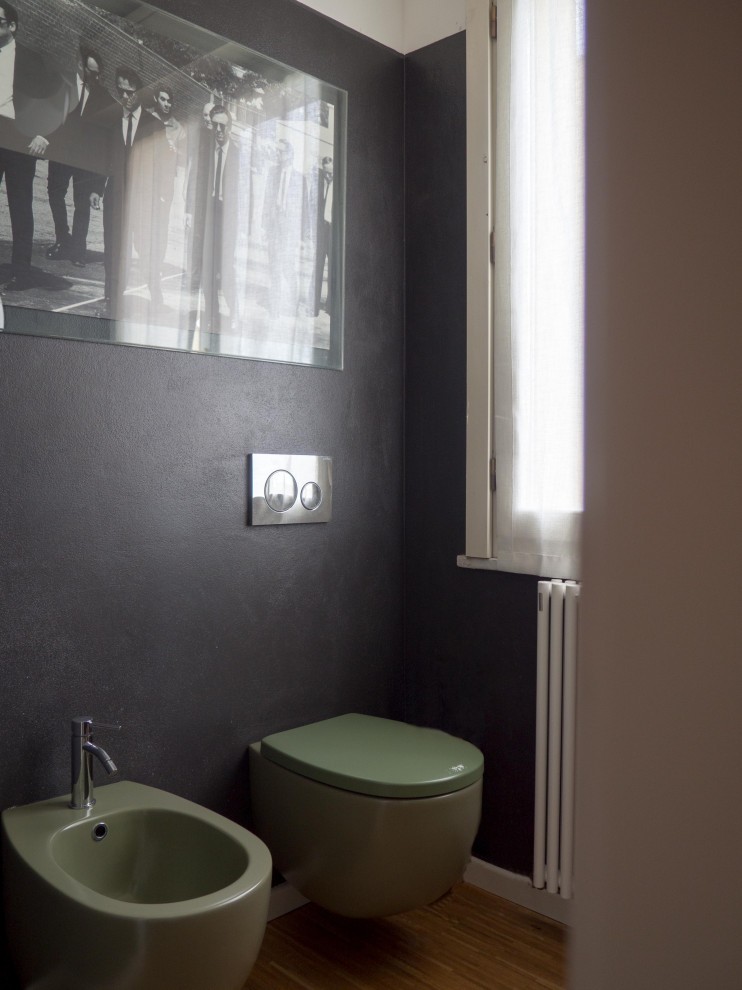 Cette photo montre un petit WC et toilettes éclectique en bois clair avec WC séparés, un mur noir, parquet clair, une vasque et meuble-lavabo suspendu.