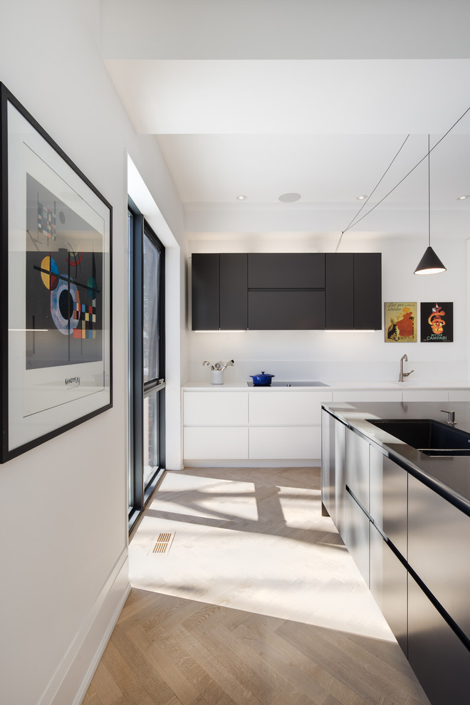 Design ideas for a mid-sized contemporary galley separate kitchen in Toronto with an integrated sink, flat-panel cabinets, white cabinets, solid surface benchtops, white splashback, glass sheet splashback, panelled appliances, light hardwood floors and with island.