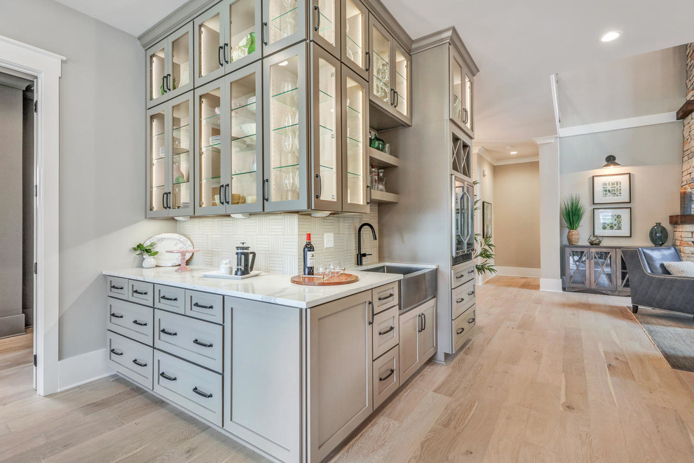 This is an example of a large arts and crafts l-shaped wet bar in Richmond with shaker cabinets, beige cabinets, quartz benchtops, beige splashback, ceramic splashback, light hardwood floors and white benchtop.