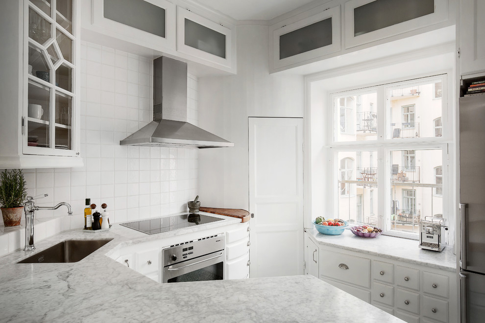 Design ideas for a mid-sized scandinavian u-shaped separate kitchen in Stockholm with a drop-in sink, raised-panel cabinets, white cabinets, marble benchtops, white splashback, porcelain splashback, stainless steel appliances and no island.