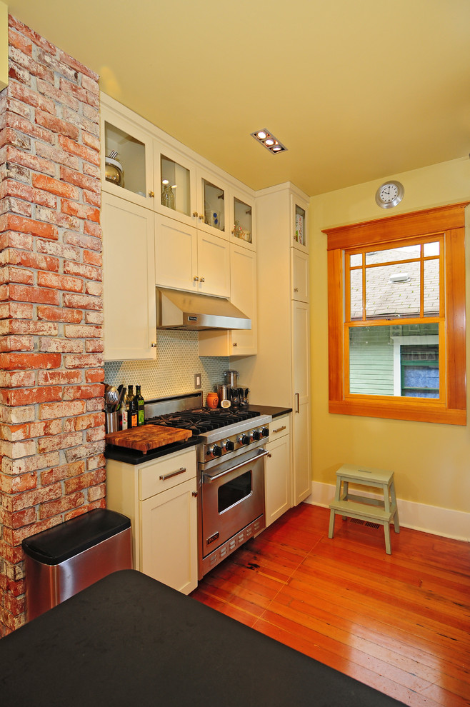 Inspiration for a small transitional u-shaped medium tone wood floor eat-in kitchen remodel in Seattle with an undermount sink, glass-front cabinets, white cabinets, white backsplash, ceramic backsplash, stainless steel appliances, yellow walls and no island