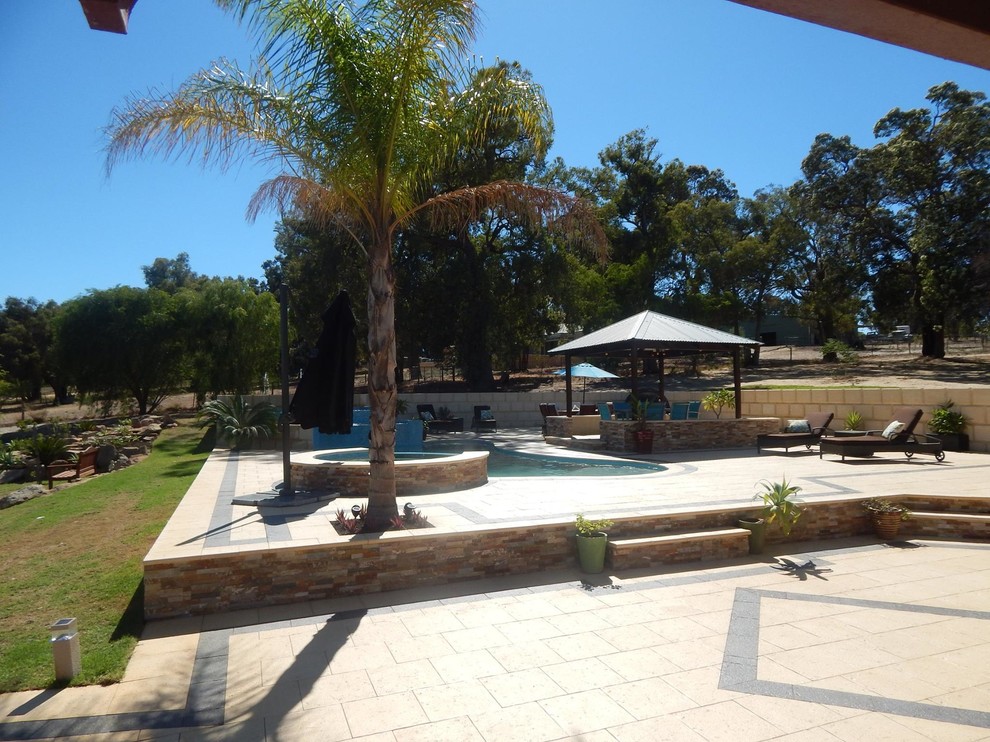 Large modern backyard custom-shaped pool in Perth with a water feature and natural stone pavers.