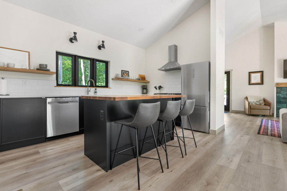 Bild på ett mellanstort funkis grå grått kök, med en enkel diskho, släta luckor, svarta skåp, marmorbänkskiva, vitt stänkskydd, stänkskydd i keramik, rostfria vitvaror, vinylgolv, en köksö och brunt golv