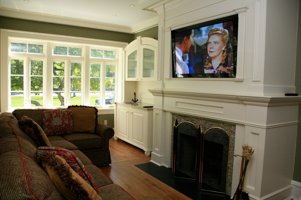 Photo of a mid-sized traditional enclosed family room in New York with a home bar, green walls, medium hardwood floors, a standard fireplace, a wood fireplace surround, a built-in media wall and brown floor.