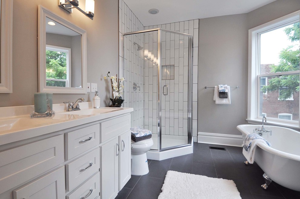 Design ideas for a large traditional master bathroom in St Louis with shaker cabinets, white cabinets, a claw-foot tub, white tile, grey walls, a two-piece toilet, porcelain floors, an integrated sink, solid surface benchtops, a corner shower, subway tile, black floor, a hinged shower door and white benchtops.