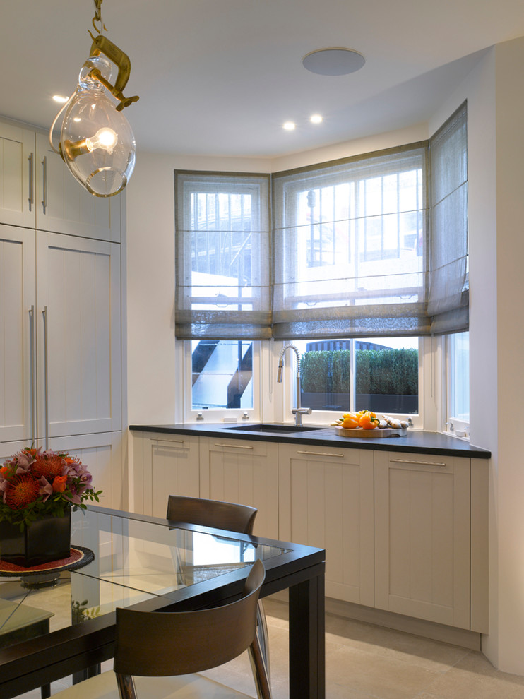 Inspiration for a large contemporary open plan kitchen in London with recessed-panel cabinets, grey cabinets, granite worktops, grey splashback, glass sheet splashback, a breakfast bar, grey floors and black worktops.