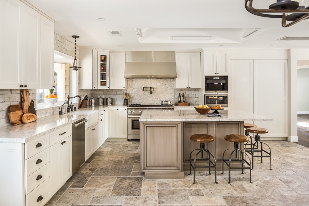 Design ideas for a large transitional l-shaped kitchen in San Francisco with a farmhouse sink, recessed-panel cabinets, white cabinets, quartz benchtops, porcelain splashback, stainless steel appliances, travertine floors, with island, multi-coloured floor, grey splashback and grey benchtop.