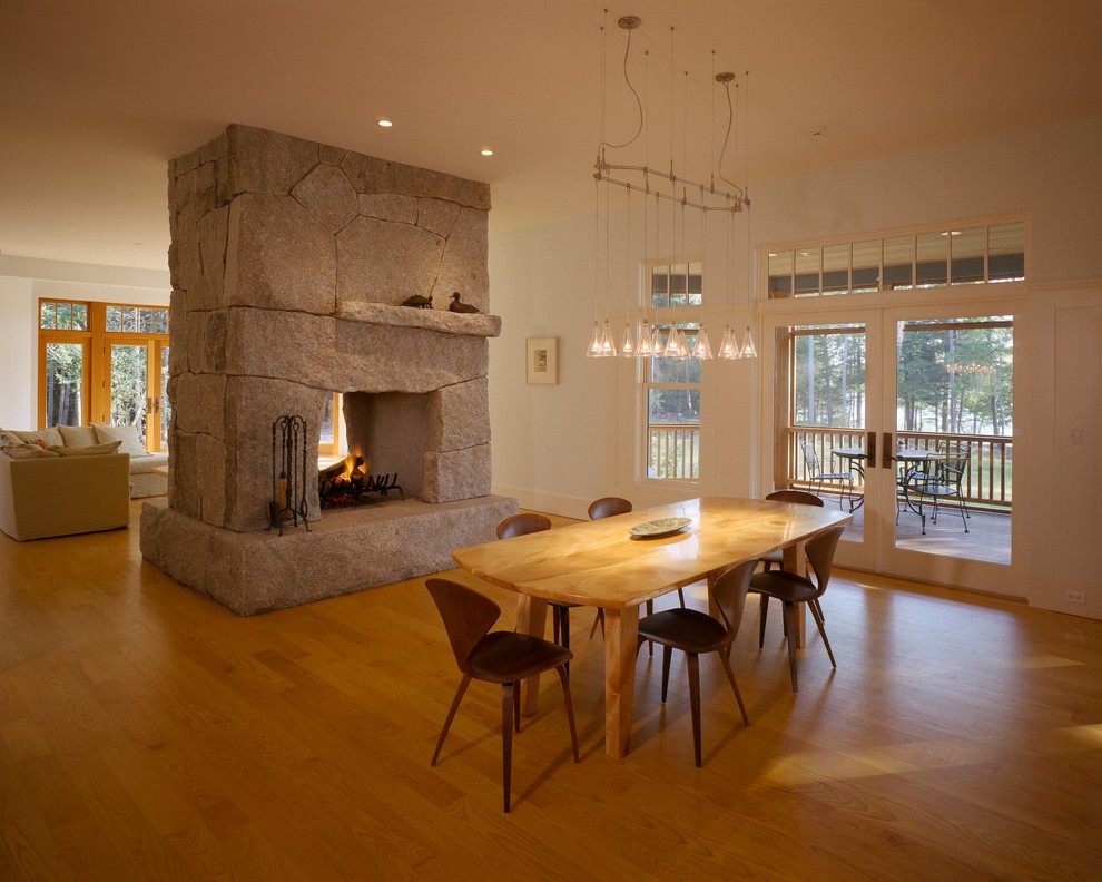 Design ideas for a large transitional open plan dining in Other with white walls, light hardwood floors, a two-sided fireplace and a stone fireplace surround.