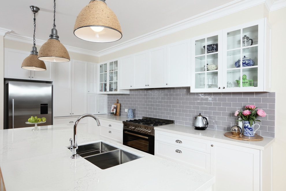 This is an example of a mid-sized transitional l-shaped eat-in kitchen in Melbourne with an undermount sink, shaker cabinets, white cabinets, quartz benchtops, grey splashback, subway tile splashback, black appliances, medium hardwood floors and with island.