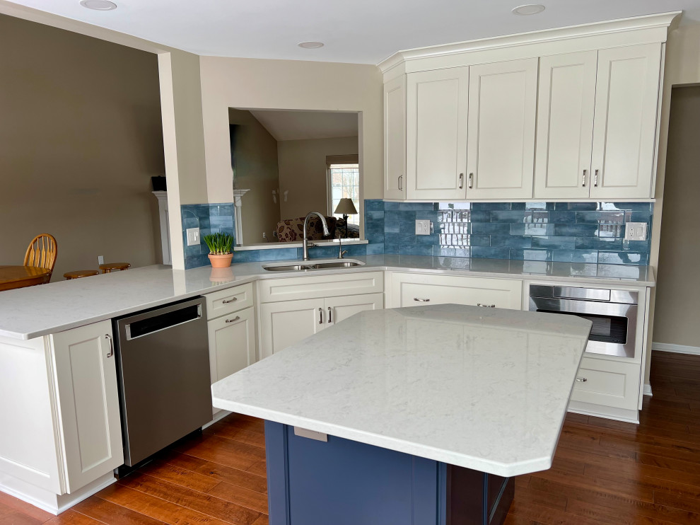 Inspiration for a mid-sized transitional u-shaped eat-in kitchen in Cincinnati with an undermount sink, recessed-panel cabinets, white cabinets, quartz benchtops, blue splashback, glass tile splashback, stainless steel appliances, medium hardwood floors, with island, brown floor and white benchtop.