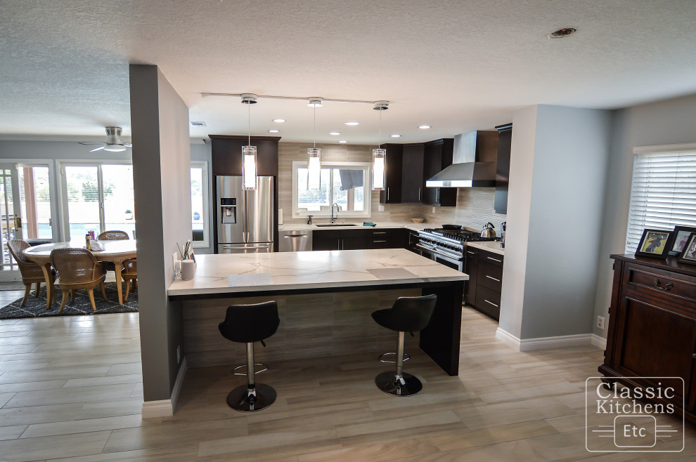 This is an example of a large modern l-shaped eat-in kitchen in Orange County with an undermount sink, shaker cabinets, dark wood cabinets, quartzite benchtops, beige splashback, ceramic splashback, stainless steel appliances, laminate floors, with island, beige floor and white benchtop.