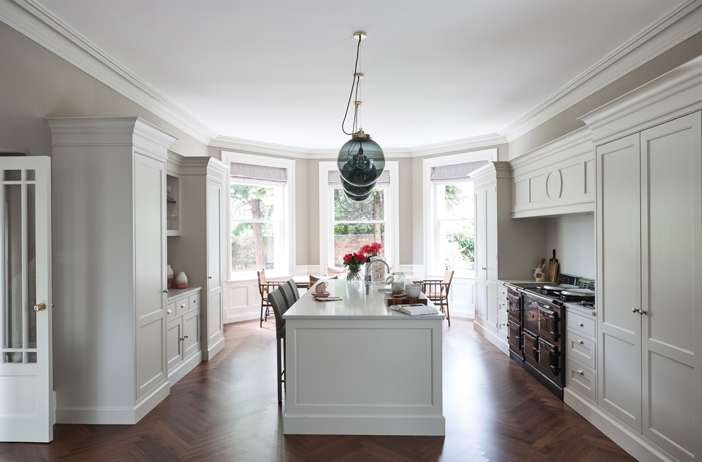 Large traditional galley eat-in kitchen in London with shaker cabinets, quartzite benchtops, black appliances, dark hardwood floors, white cabinets, with island, brown floor and white benchtop.