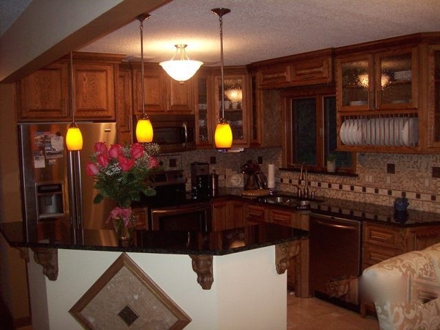 Enclosed kitchen - large galley light wood floor enclosed kitchen idea in Cedar Rapids with a drop-in sink, raised-panel cabinets, medium tone wood cabinets, multicolored backsplash, stainless steel appliances and an island