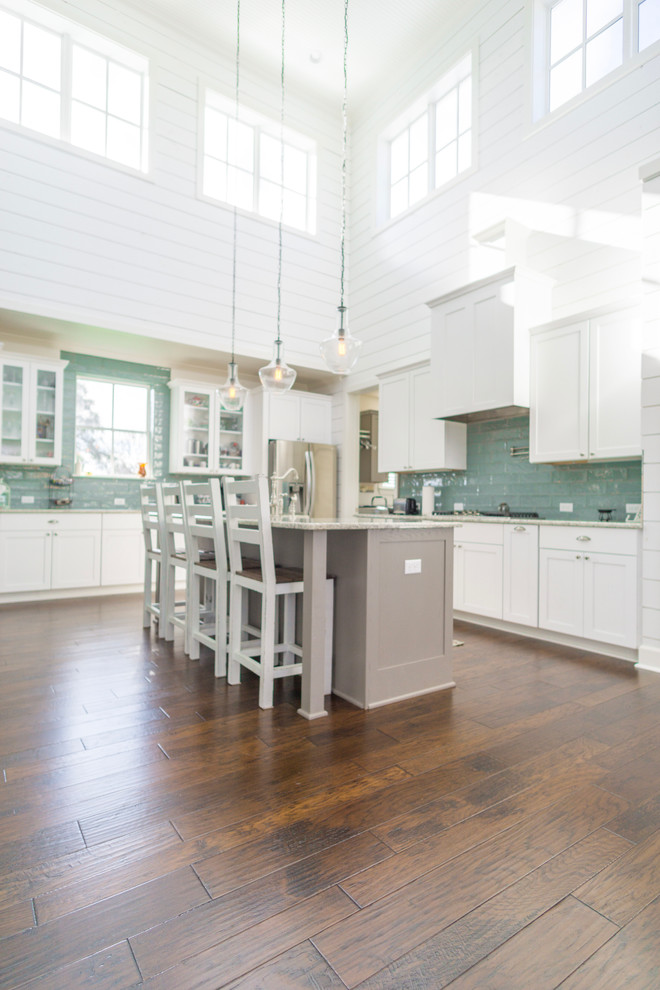 This is an example of a large country eat-in kitchen in Austin with a farmhouse sink, shaker cabinets, white cabinets, quartz benchtops, blue splashback, glass tile splashback, stainless steel appliances, medium hardwood floors and with island.