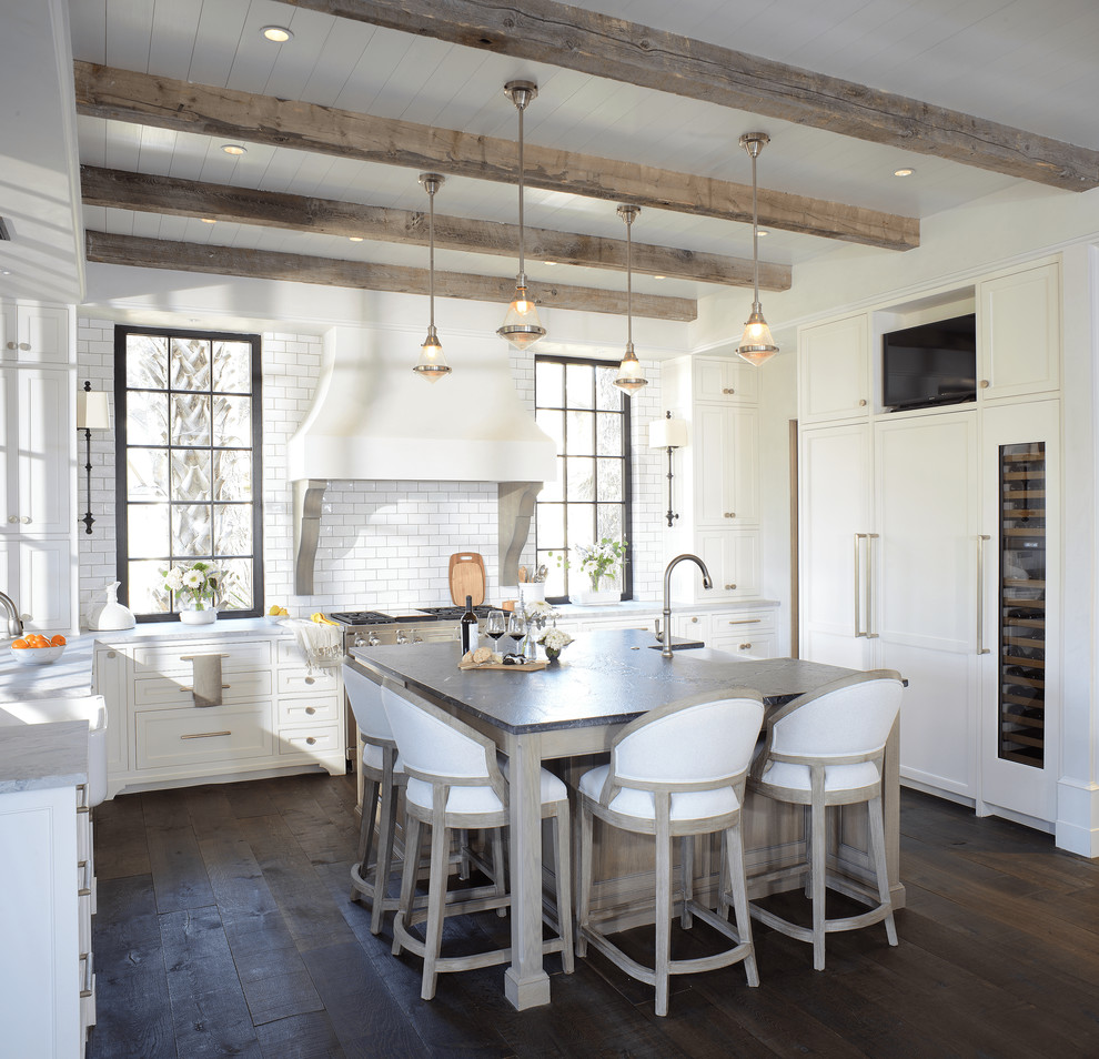 Photo of a beach style u-shaped kitchen in Charleston with a farmhouse sink, shaker cabinets, white cabinets, white splashback, subway tile splashback, panelled appliances, dark hardwood floors, with island, brown floor and grey benchtop.