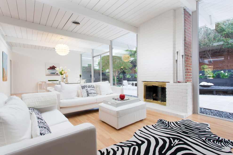 This is an example of a midcentury formal open concept living room in San Francisco with white walls, light hardwood floors, a standard fireplace and a brick fireplace surround.