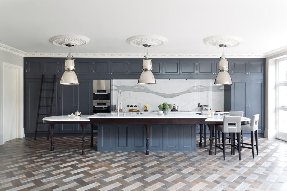 Traditional galley kitchen in London with beaded cabinets, blue cabinets, white splashback, stainless steel appliances, an island and marble splashback.