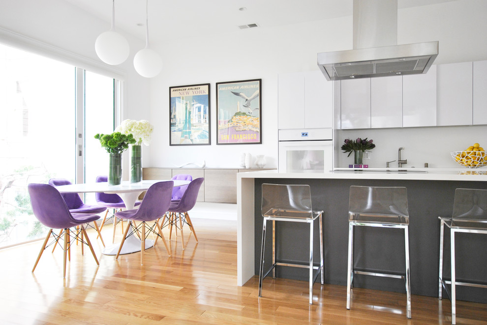 This is an example of a mid-sized contemporary eat-in kitchen in San Francisco with flat-panel cabinets, white cabinets, solid surface benchtops, medium hardwood floors, with island and brown floor.