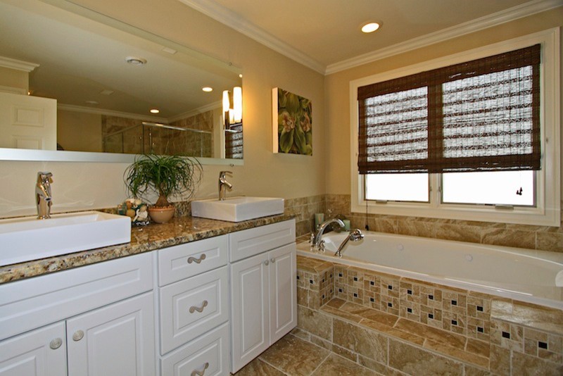 Transitional bathroom in Chicago with a vessel sink, raised-panel cabinets, white cabinets, granite benchtops, a drop-in tub, a corner shower, a two-piece toilet, beige tile and porcelain tile.