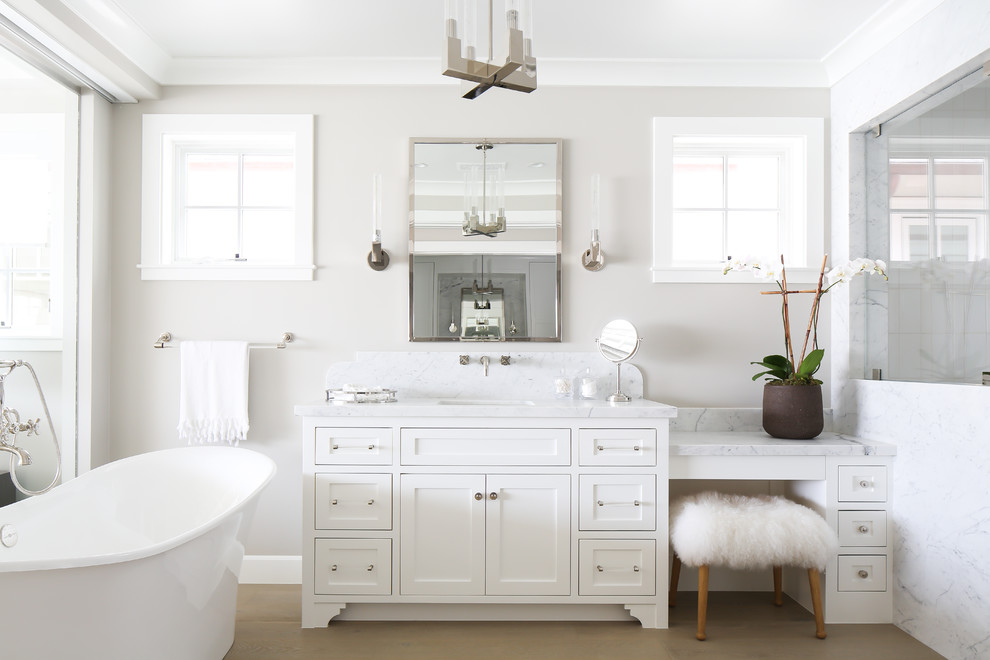 Design ideas for a beach style master bathroom in Orange County with shaker cabinets, white cabinets, a freestanding tub, grey walls and light hardwood floors.
