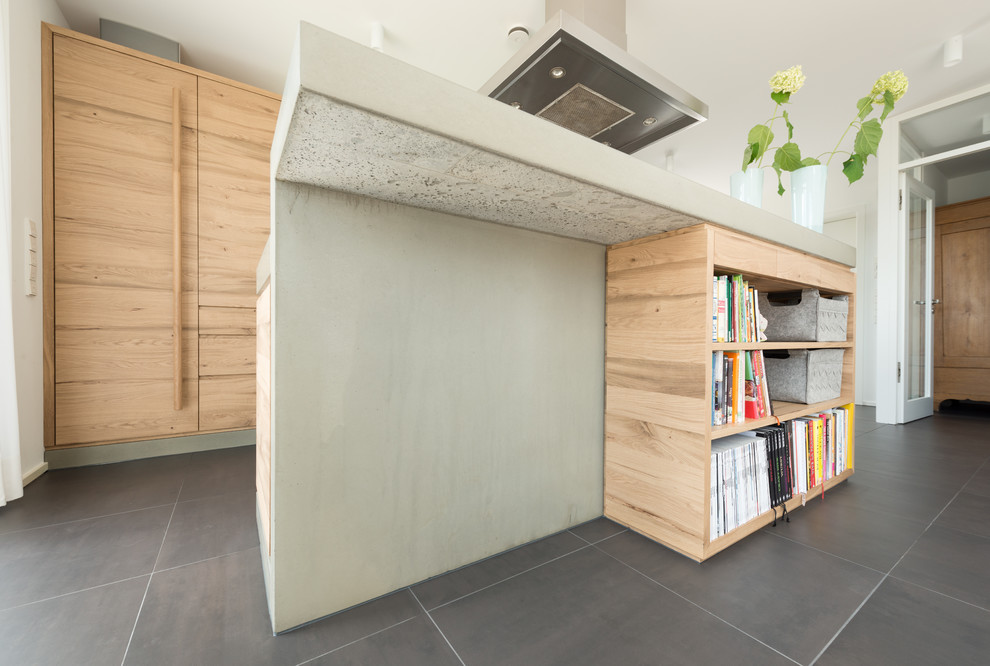 Photo of a mid-sized contemporary single-wall open plan kitchen in Other with a single-bowl sink, flat-panel cabinets, light wood cabinets, concrete benchtops, white splashback, with island, grey floor, black appliances and ceramic floors.