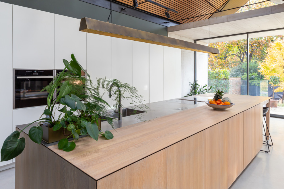 This is an example of an expansive scandi open plan kitchen in London with flat-panel cabinets, white cabinets, stainless steel worktops, an island and multicoloured worktops.
