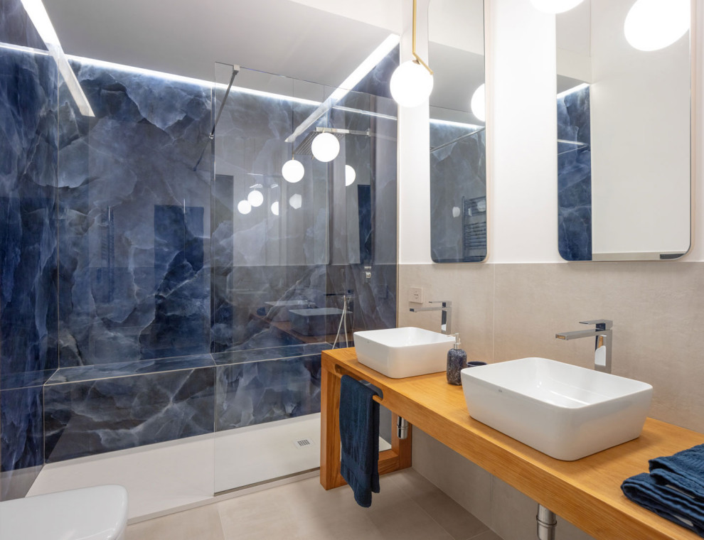 Idéer för stora funkis brunt en-suite badrum, med en kantlös dusch, en toalettstol med separat cisternkåpa, porslinskakel, vita väggar, klinkergolv i porslin, ett fristående handfat, träbänkskiva, beiget golv, öppna hyllor, skåp i ljust trä, blå kakel och med dusch som är öppen