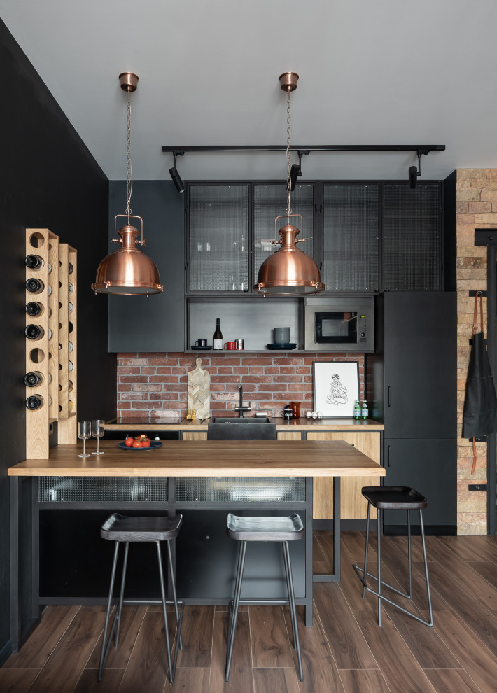 Design ideas for a small industrial single-wall open plan kitchen in Saint Petersburg with a drop-in sink, glass-front cabinets, black cabinets, wood benchtops, black splashback, timber splashback, black appliances, porcelain floors, with island, brown floor and yellow benchtop.