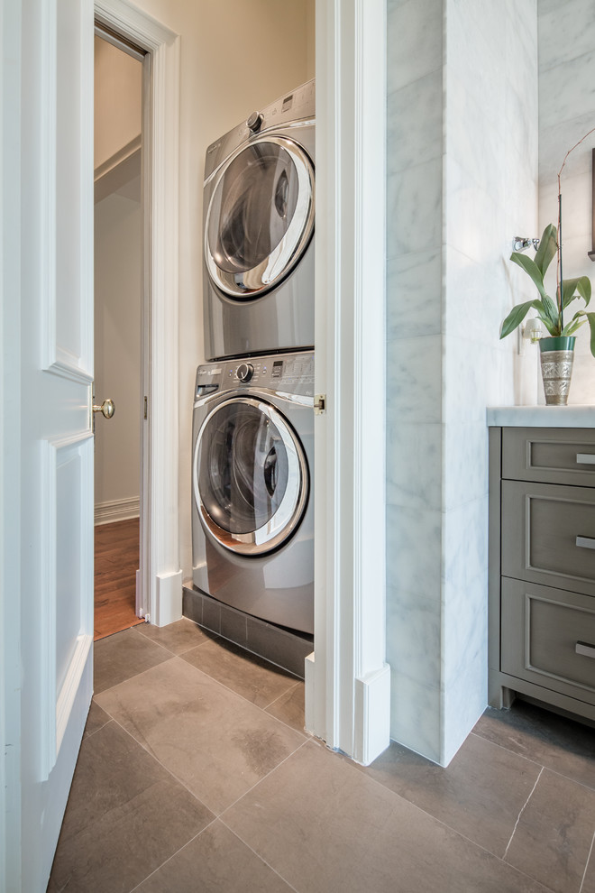 Small transitional dedicated laundry room in Miami with an undermount sink, recessed-panel cabinets, grey cabinets, marble benchtops, white walls, marble floors and a stacked washer and dryer.