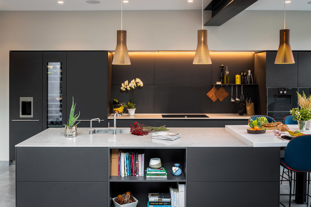 Photo of a contemporary galley kitchen in London with an undermount sink, flat-panel cabinets, black cabinets, black splashback, with island and white benchtop.
