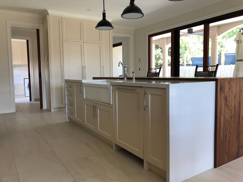 Inspiration for a large traditional galley open plan kitchen in Melbourne with a farmhouse sink, shaker cabinets, beige cabinets, quartz benchtops, white splashback, porcelain splashback, black appliances and with island.
