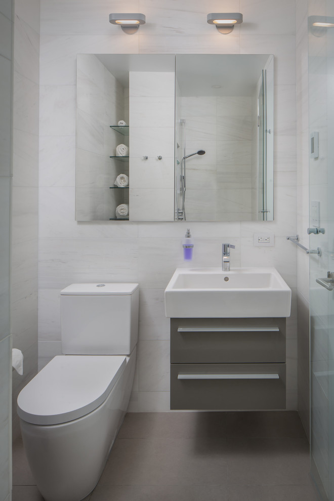 Design ideas for a small contemporary 3/4 bathroom in New York with flat-panel cabinets, grey cabinets, a corner shower, a two-piece toilet, white tile, porcelain tile, white walls, ceramic floors, a drop-in sink, grey floor, a hinged shower door and white benchtops.