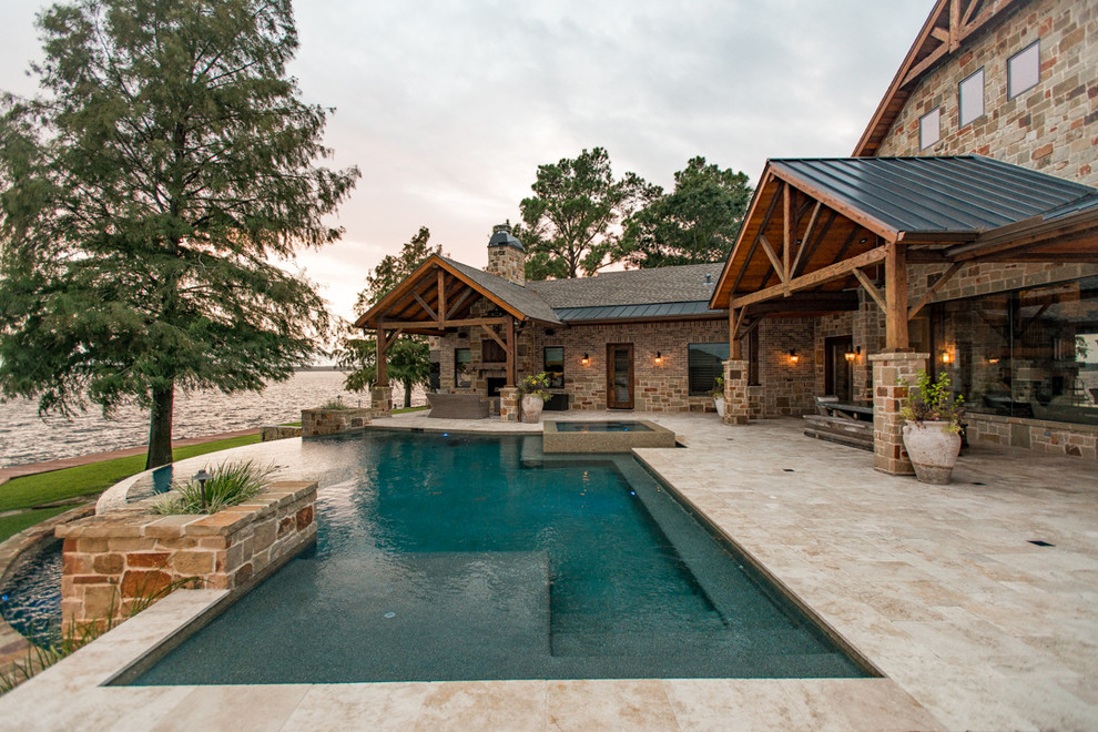 This is an example of a large country backyard custom-shaped infinity pool in Houston with a hot tub and natural stone pavers.