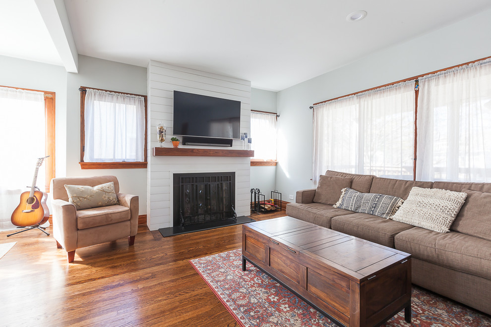 Design ideas for a country open concept family room in Chicago with grey walls, medium hardwood floors, a standard fireplace, a wood fireplace surround, a wall-mounted tv and brown floor.