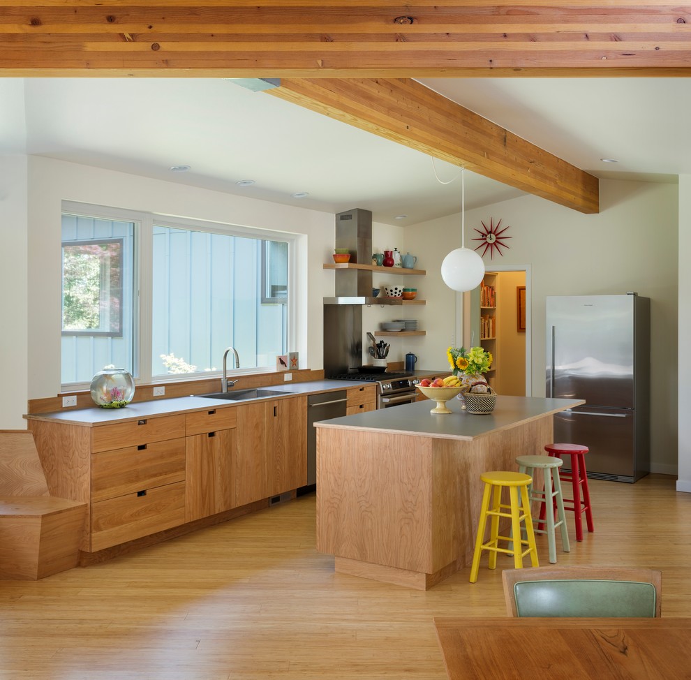 Photo of a midcentury l-shaped open plan kitchen in Seattle with with island, flat-panel cabinets, medium wood cabinets, laminate benchtops, stainless steel appliances, a drop-in sink and medium hardwood floors.