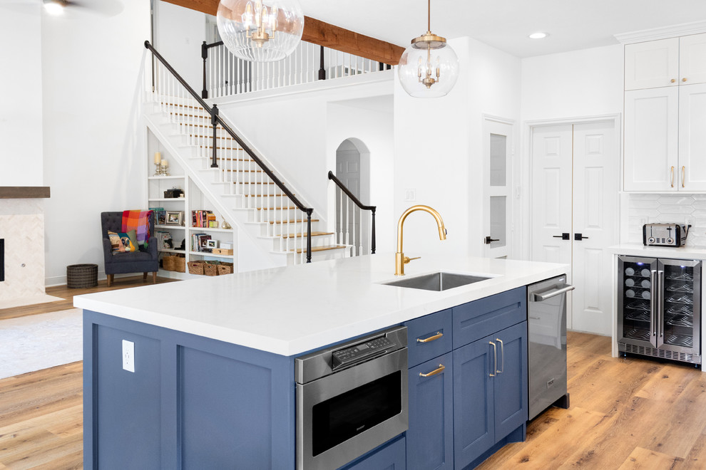 Mid-sized transitional l-shaped eat-in kitchen in Houston with an undermount sink, recessed-panel cabinets, blue cabinets, quartz benchtops, white splashback, subway tile splashback, stainless steel appliances, light hardwood floors, with island, orange floor and white benchtop.