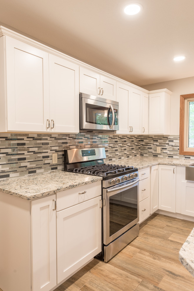 Example of a mid-sized transitional l-shaped medium tone wood floor and brown floor eat-in kitchen design in Minneapolis with a farmhouse sink, shaker cabinets, white cabinets, granite countertops, multicolored backsplash, matchstick tile backsplash, stainless steel appliances, an island and gray countertops