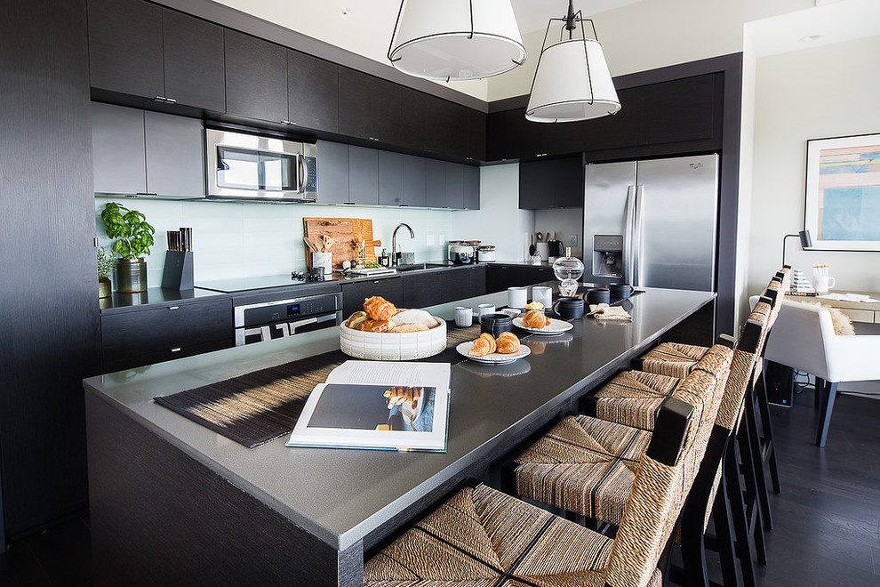 Penthouse Decor in Bethesda - Mid-sized transitional l-shaped dark wood floor and black floor open concept kitchen photo in DC Metro with an undermount sink, flat-panel cabinets, black cabinets, solid surface countertops, white backsplash, glass tile backsplash, stainless steel appliances and an island