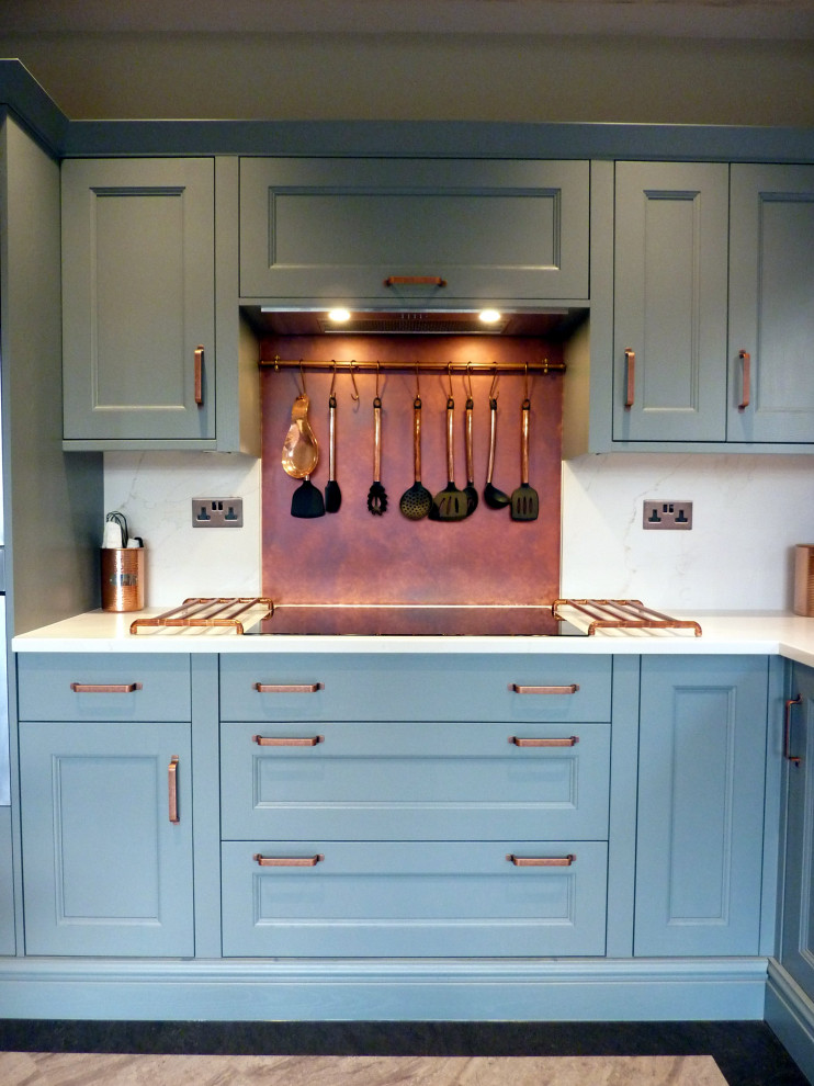 Klassisk inredning av ett stort vit vitt kök, med en rustik diskho, luckor med profilerade fronter, blå skåp, bänkskiva i kvartsit, orange stänkskydd, svarta vitvaror, vinylgolv, en köksö och grått golv