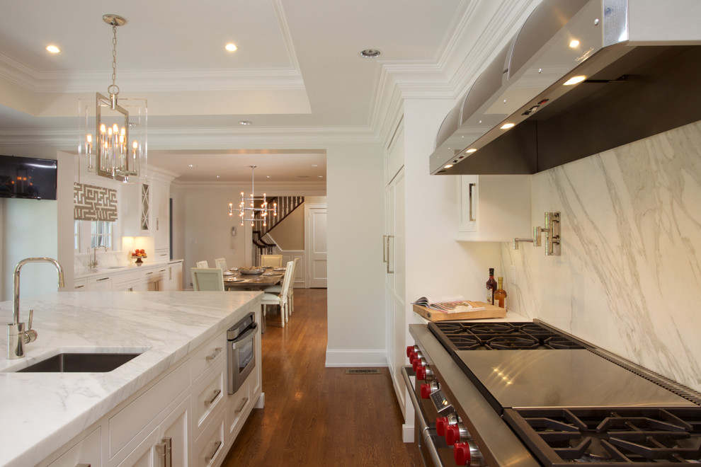 Large transitional u-shaped medium tone wood floor eat-in kitchen photo in New York with white cabinets, marble countertops, stone slab backsplash, paneled appliances, an island, an undermount sink and recessed-panel cabinets