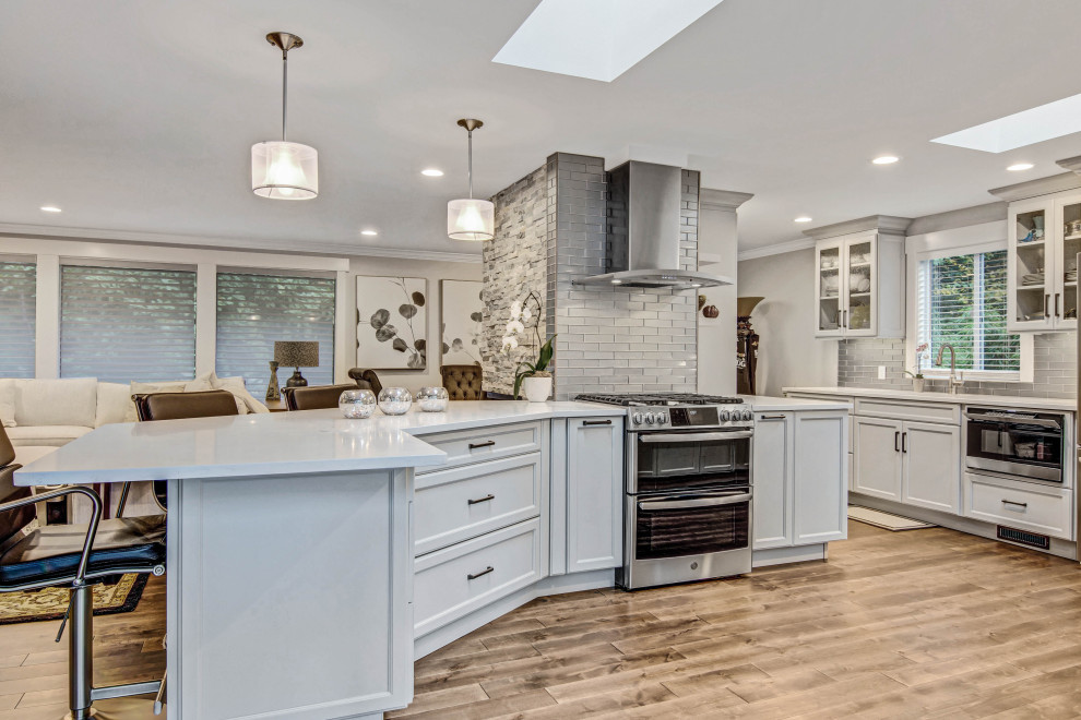 Open concept kitchen - transitional medium tone wood floor and brown floor open concept kitchen idea in Seattle with an undermount sink, recessed-panel cabinets, gray cabinets, quartz countertops, gray backsplash, subway tile backsplash, stainless steel appliances, a peninsula and white countertops