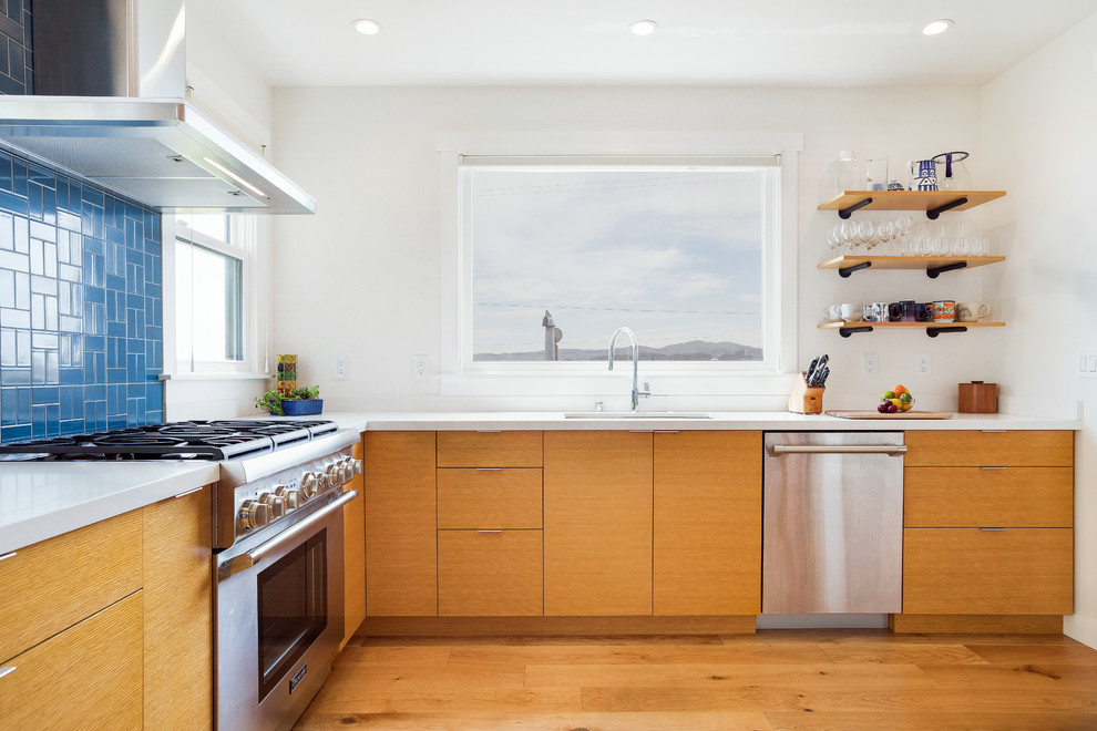 Photo of a mid-sized midcentury u-shaped open plan kitchen in San Francisco with an undermount sink, blue splashback, stainless steel appliances, no island, brown floor, white benchtop, flat-panel cabinets, medium wood cabinets, ceramic splashback, medium hardwood floors and solid surface benchtops.