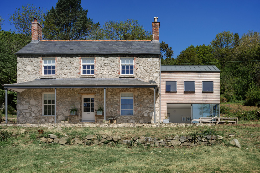 This is an example of a large country two-storey beige house exterior in Devon with stone veneer and a gable roof.