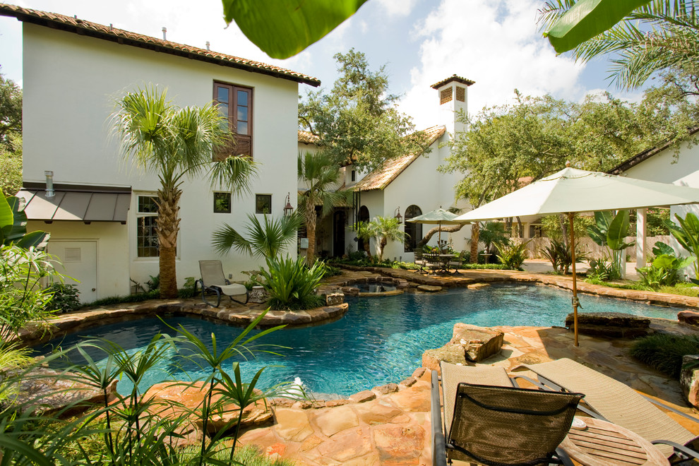 Photo of a large tropical backyard custom-shaped lap pool in Austin with a hot tub and natural stone pavers.