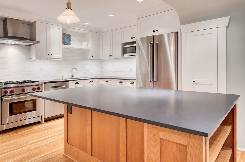 Mid-sized arts and crafts l-shaped open plan kitchen in Seattle with a drop-in sink, shaker cabinets, white cabinets, quartz benchtops, white splashback, marble splashback, stainless steel appliances, light hardwood floors, with island and brown floor.