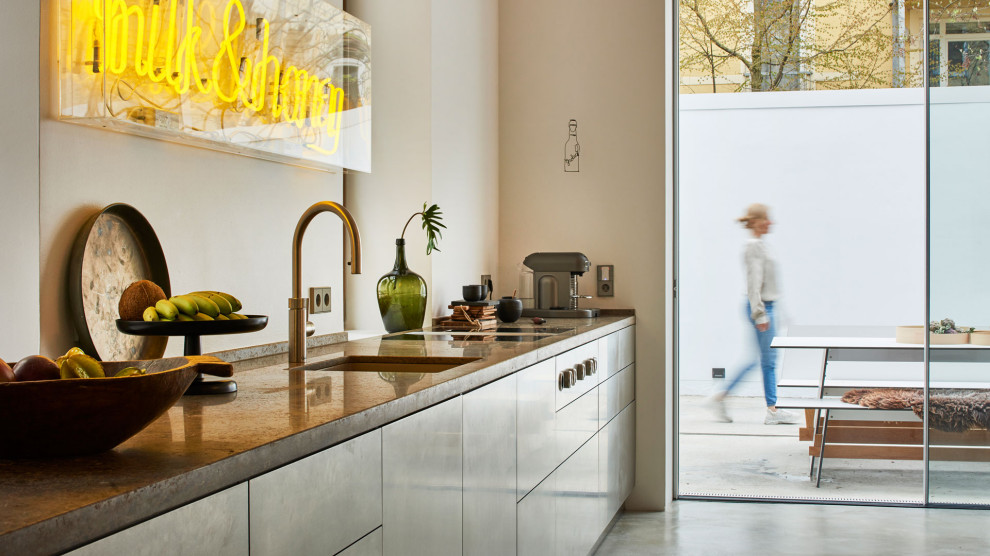 Immagine di una cucina lineare moderna con ante lisce, ante in acciaio inossidabile, top in granito, paraspruzzi bianco, elettrodomestici neri, pavimento grigio, top beige e travi a vista